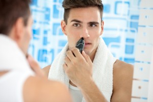 handsome young man remove hair from his nose with trimmer